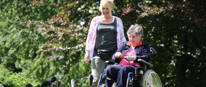 Bild vergrößern: alte Dame im Rollstuhl mit Pflegebegleitung