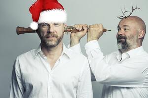 Ansicht von zwei Männern, der Linksstehende trägt eine Weihnachtsmütze, der Rechtsstehende ein kleines Geweih und schiebt ihm scheinbar spaßeshalber eine Klarinette durch den Kopf. 