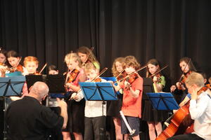 Junge Musiker (Streicher), links im Vordergrund ein Dirigent. 