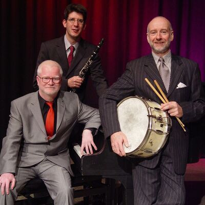 Bild vergr&ouml;&szlig;ern: Drei M&auml;nner, zwei davon haben ein Instrument in der Hand: ein Schlagzeug und eine Klarinette.