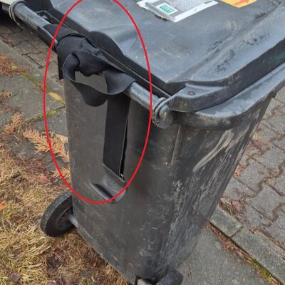 Bild vergr&ouml;&szlig;ern: Das Foto zeigt ein Abfalltonne, die mit einem Gurt versehen ist.