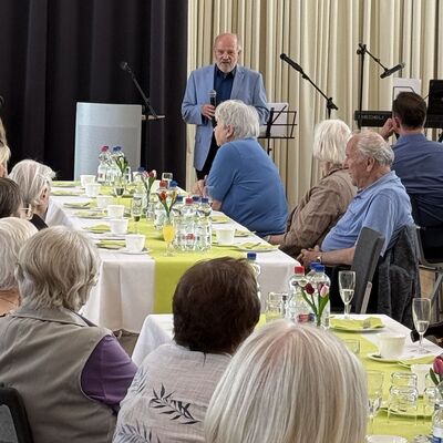 Bild vergr&ouml;&szlig;ern: Das Foto zeigt den Vorsitzenden des Seniorenbeirats, Lothar Jerzembek, der vor den G&auml;sten der nachgeholten Seniorenweihnachtsfeier im Juni 2026 im B&uuml;rgersaal eine kurze Anspr&auml;che h&auml;lt