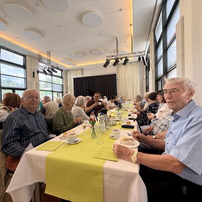 Bild vergr&ouml;&szlig;ern: Das Foto zeigt Seniorinnen und Senioren an einem gedeckten Tisch bei der nachgeholten Seniorenweihnachtsfeier im Juni 2026 im B&uuml;rgersaal