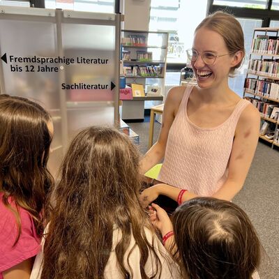 Bild vergr&ouml;&szlig;ern: Das Bild zeigt eine lachende Mitarbeiterin der Bibliothek Kleinmachnow mit drei Kindern
