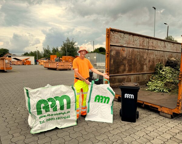 Das Foto zeigt einen APM-Mitarbeiter auf einem Wertstoffhof mit einer Biotonne und zwei Bigbags