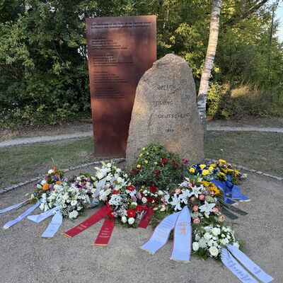 Bild vergr&ouml;&szlig;ern: Das Foto zeigt Gedenkkr&auml;nze vor dem Gedenkstein am Adam-Kuckhoff-Platz