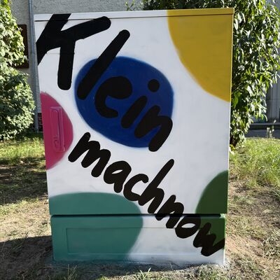 Bild vergr&ouml;&szlig;ern: Das Foto zeigt einen von Sch&uuml;lerinnen und Sch&uuml;lern der Klasse 6a der Grundschule Auf dem Seeberg gestalteten Stromkasten mit bunten Punkten und Kleinmachnow-Schriftzug.