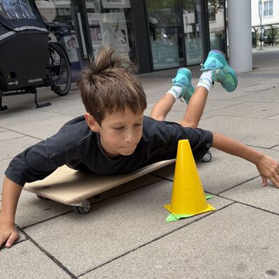 Bild vergr&ouml;&szlig;ern: Das Foto zeigt einen Jungen, der beim Sportlichern Aktionstag rund ums Rathaus am 5. September 2026 auf einem Brett mit Rollen &uuml;ber den Gehweg rollt