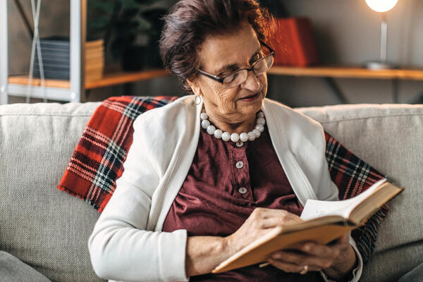 Bild vergrößern: Alte Dame sitzt auf dem Sofa und liest ein Buch